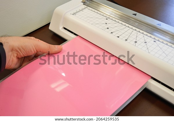 Worker laminating pouches with a pink sheet inside\
on an office table.