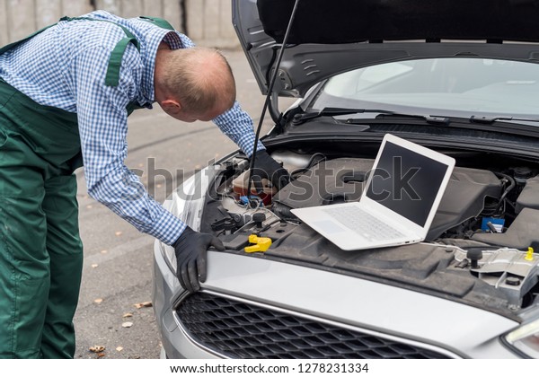 Worker with\
laptop making diagnostic of car\
engine