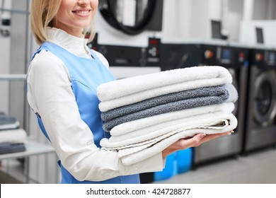 Worker Laundry girl holding fresh towels in her hands and smiles at the dry cleaners