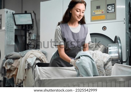 Worker of laundry shop loading industrial washing machine with clothes