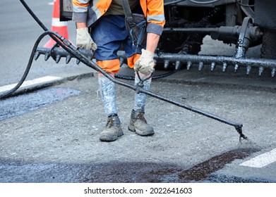 Worker lay bitumen using tar sprayer, standing in front of a bitumen spraying machine.