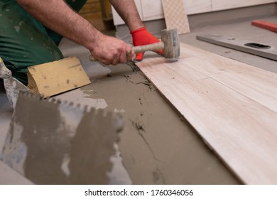 A worker laying ceramic tiles in the bathroom with a rubber mallet gently aligns the floor plane.