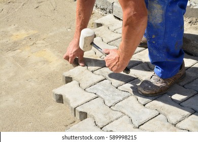 Worker laying concrete pavement onto the bedding sand and tapping them with a wooden hammer. Motion blur on hammer.
