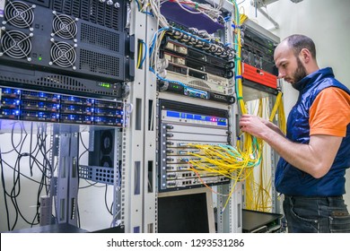 Worker Lays Telecommunication Cables In The Server Room. A Man Twists The Wires In A Modern Data Center. A Technician Connects Internet Backbones With A Central Router.