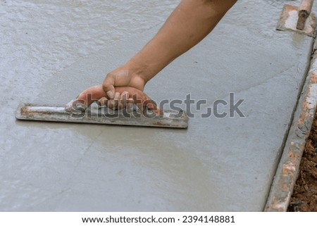 Worker leveling fresh concrete pavement with wet cement using special working tool