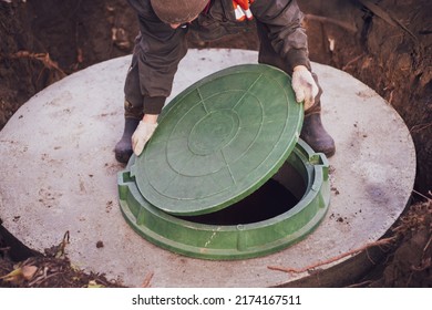 A worker lifts the manhole cover of a sewer well. Construction and maintenance of septic tanks in the village. - Shutterstock ID 2174167511