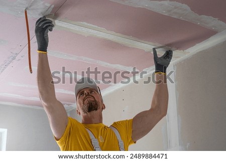 The worker make a plasterboard ceiling. He does taping plaster drywall ceiling joints. A red plasterboard improve the fire resistance of ceiling structures.