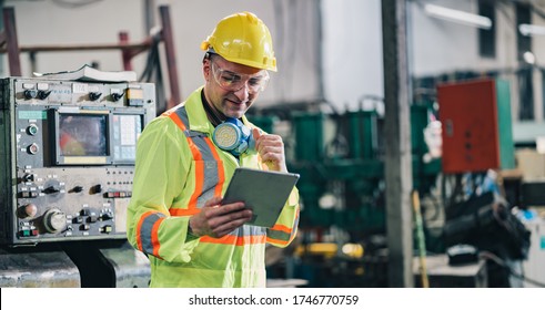 Worker Man Caucasian Happy Smiling In Protective Safety Jumpsuit Uniform With Yellow Hardhat And Using Tablet At Factory.Metal Working Industry Concept Professional Engineer Manufacturing Workshop