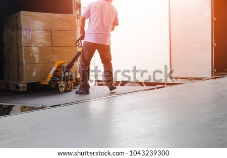 Worker man dragging hand pallet truck or manual forklift with the shipment pallet unloading from a truck.
