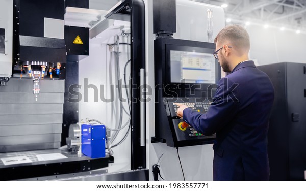 Worker man entering data in CNC drill machine at\
automatic factory floor. Modern process metal detail production\
going for car.