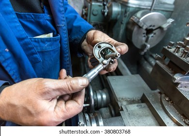 worker man hand measuring with micrometer in a workshop beside the turning machine
