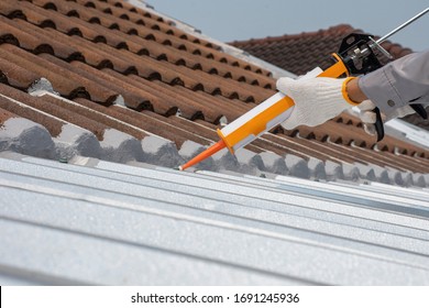 Worker man hand using glue gun with silicone adhesive or manual caulking gun with polyurethane to fix the metal steel on the roof. Installing and building construction concept.