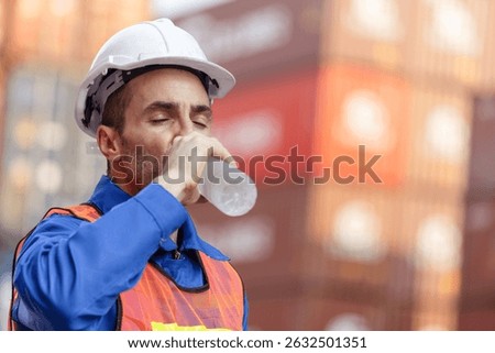 Worker man in hard hat drinking water at containers cargo blurred background