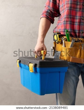 Worker man holding construction toolbox near concrete or cement wall. Male hand and tool box for house room renovation. Home renovation concept