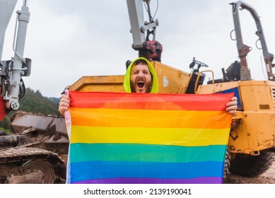 Worker Man On A Construction Site Shouts While Holding A Rainbow Lgbt Pride Flag. Concept Of Sexual Discrimination In Employment.