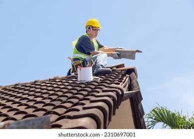 Worker man repairing eaves and tile of the old roof.