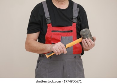 Worker Man In Uniform, Overalls And Protective Helmet Is Holding Rubber Hammer With Yellow Handle On White Background.