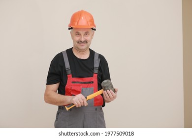 Worker Man In Uniform, Overalls And Protective Helmet Is Holding Rubber Hammer With Yellow Handle On White Background.