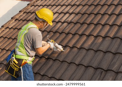 Worker man using silicone sealant adhesive  to fix crack of the old tile roof. - Powered by Shutterstock