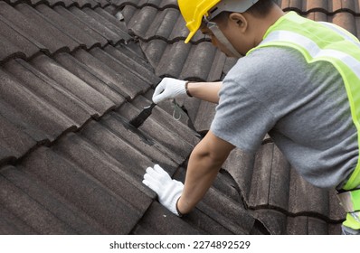 Worker man using waterproof roof coating repair to fix crack of the old tile roof.