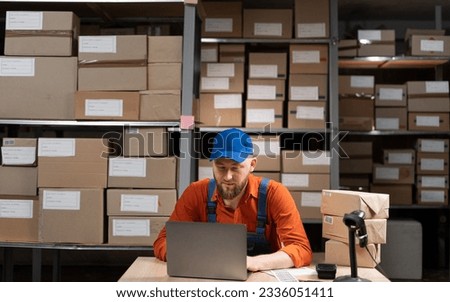Worker manager checking on merchandise, working on laptop computer in warehouse facility. Copy space