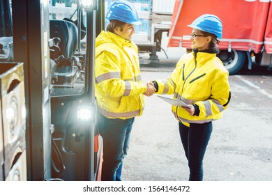 Worker And Manager Shaking Hands At Distribution Center Behind A Forklift