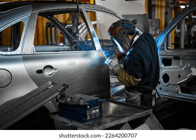 Worker in mask welds metal parts of auto carcass in shop - Shutterstock ID 2264200707