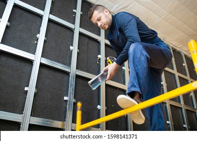 Worker Measures The Metal Detail. Assembling Metal Frame Of Wall. Make Soundproofing In Room. Renovation At Home. Building Construction Indoor. 

