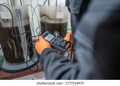 Worker Measures The Quality Of The Water With Gloves And A Digital Measurement Tool At A Waste Water Treatment Plant
