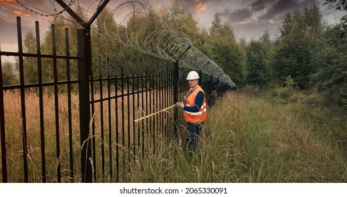 Worker with a measuring tape measure a fence with barbed wire. The concept of border closure, districts and specially protected objects. Access restriction and protection - Shutterstock ID 2065330091
