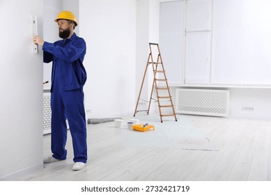 Worker measuring wall with building level indoors, space for text