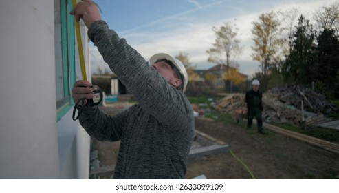 Worker measuring window frame with tape on a building under construction, precise measurements, focused craftsmanship, building progress, exterior project setup