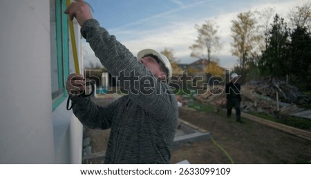 Worker measuring window frame with tape on a building under construction, precise measurements, focused craftsmanship, building progress, exterior project setup