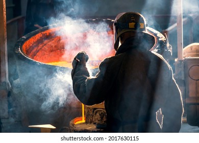 worker of metal and alloys foundry at a metallurgical plant, rear view. smoke from red metal - Powered by Shutterstock