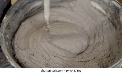 The worker mixes the mortar. Wet Concrete or motrar mixing texture. Gray mortar, concrete surface. The solution is stirred, apartment renovation.