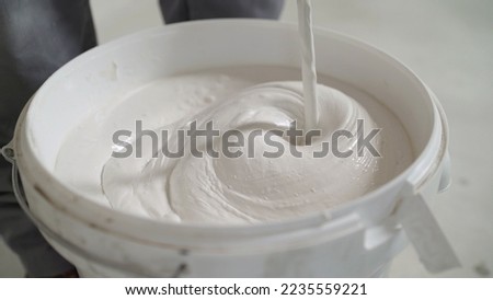 A worker mixes mortar for white tiles. Mixing mortar in a white bucket.