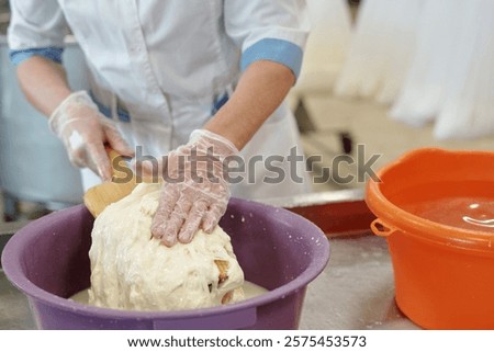 Worker mixing dough manually while wearing gloves in bakery setting, ensuring hygiene and safety during food preparation process