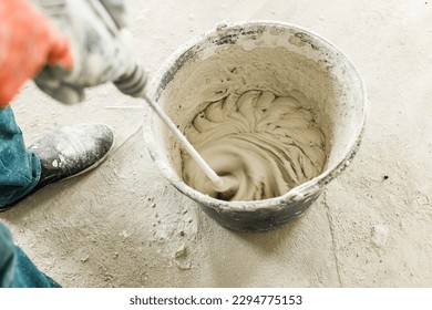 Worker mixing gypsum plaster with water for plastering walls. Construction of house and home renovation concept. Close up of bucket with stucco mix and handyman hands