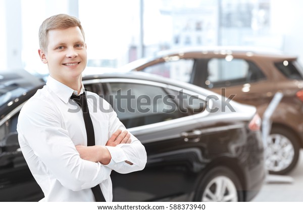 Worker of the month. Handsome young salesman smiling\
happily posing confidently with his arms crossed car dealership on\
the background copyspace profession occupation business businessman\
auto