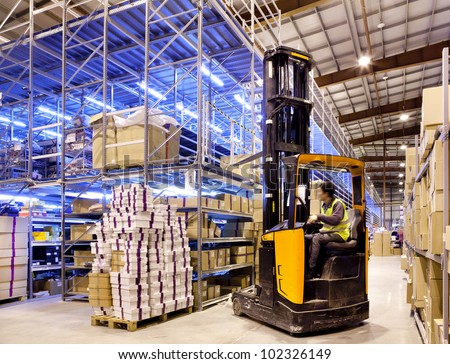 Worker in the motion on forklift in the large modern warehouse