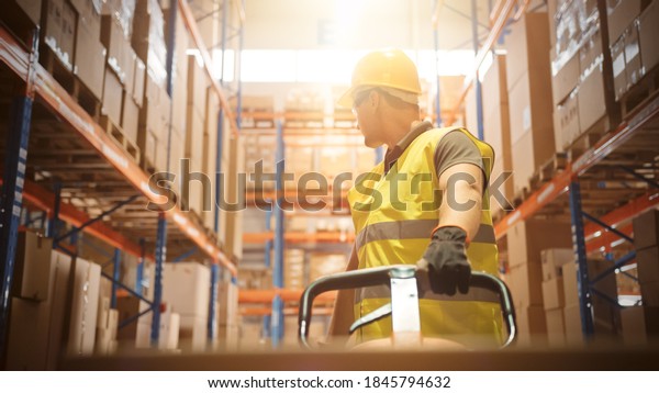 Worker
Moves Cardboard Boxes using Hand Pallet Truck, Walking between Rows
of Shelves with Goods in Retail Warehouse. People Work in Product
Distribution Logistics Center. Point of View
Shot
