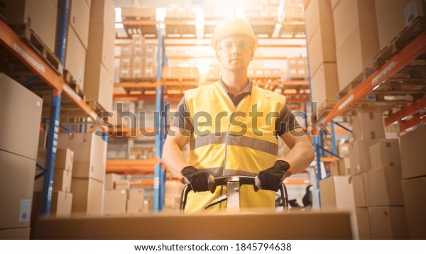 Worker\
Moves Cardboard Boxes using Hand Pallet Truck, Walking between Rows\
of Shelves with Goods in Retail Warehouse. People Work in Product\
Distribution Logistics Center. Point of View\
Shot
