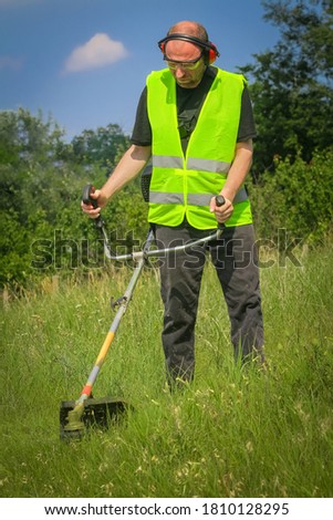 Worker mowing grass with grass trimmer