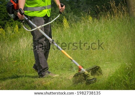 Worker mowing grass with grass trimmer