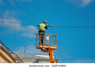 Worker On Aerial Platform Repair Broken Electric Cable At Height. Man In Hardhat Repair Damaged Wire On Truck Crane. Worker In Lift Bucket Repair Power Line