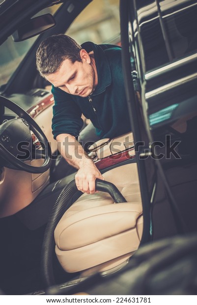 Worker on a car wash cleaning car interior with vacuum\
cleaner 