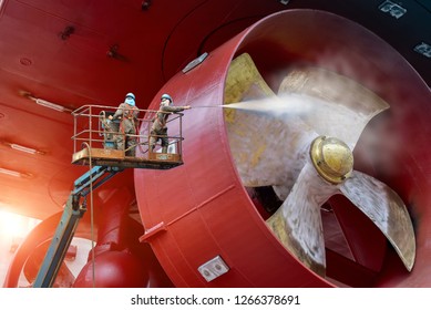 Worker On Cherry Picker Car With Safety Harness In Dry Dock Ship Cleaning By Water Jet Cleaners And Sand Blasting During Routine Overhaul On Outdated Manual Technology In Shipyard