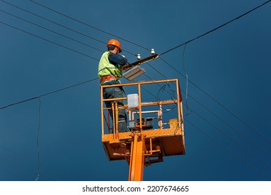 Worker On Crane Installing Led Lantern On Electric Wire At Height. Man In Lift Bucket Upgrade Street Lights, Install Led Panel On Electric Cables.  Improving Outdoor Lighting On Energy Efficient Light