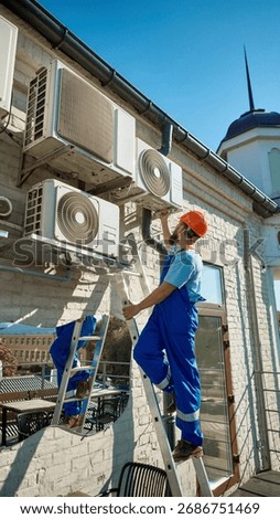 Worker on ladder maintaining multiple air conditioning units on building wall. Concept of business and service industry focused on technical maintenance and energy system efficiency.