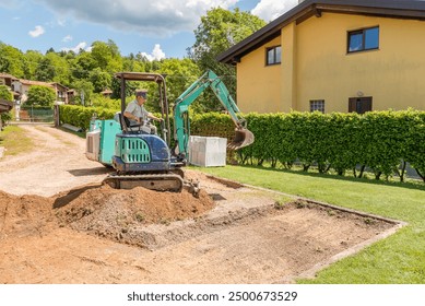 A worker on a mini excavator is digging the ground ahead of the house. Groundwork and exterior paving.